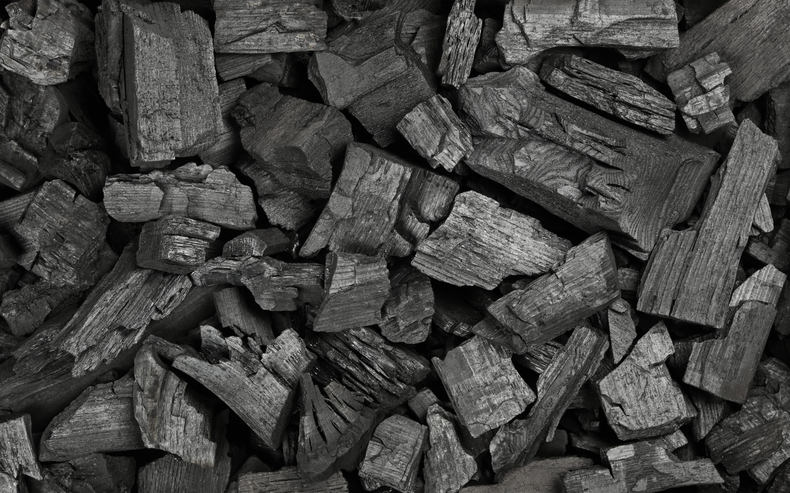 Close up background texture of many black lump charcoal pieces ready for barbecue grill, elevated top view, directly above